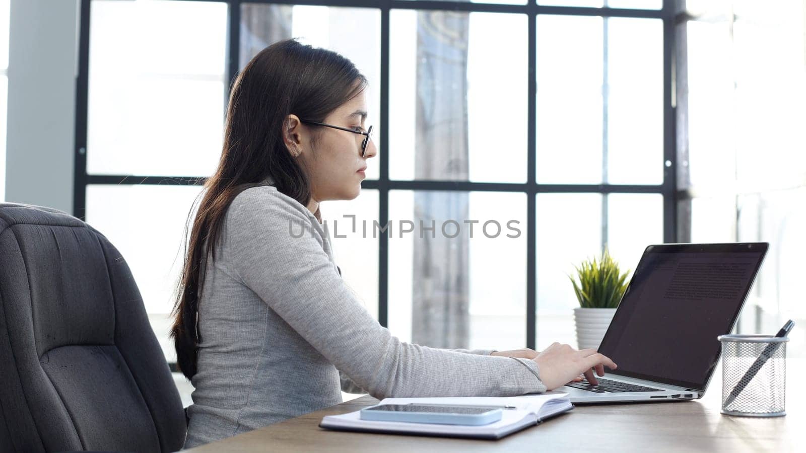 A young woman with glasses in the office is working on a laptop.