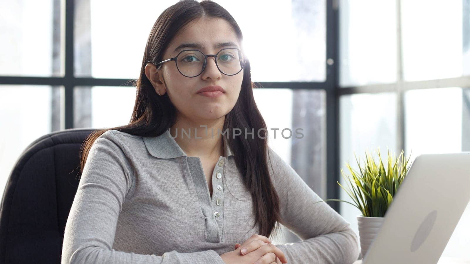 A young woman with glasses in the office looks at the camera.