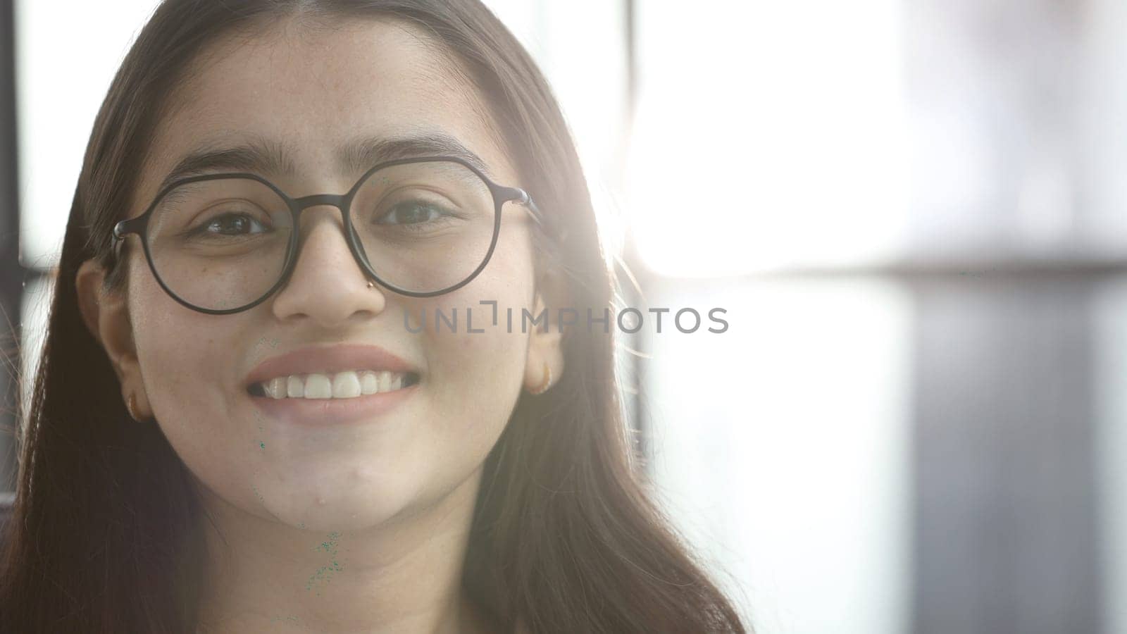 A young woman with glasses in the office looks at the camera.