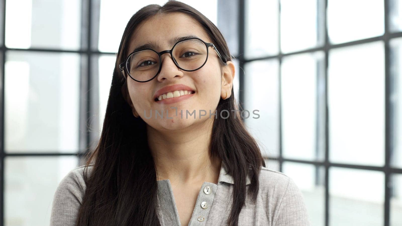 A young woman with glasses in the office looks at the camera.