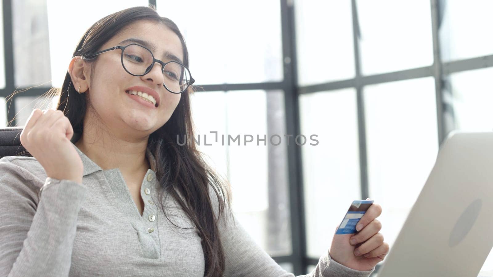 A young woman in close-up with glasses and a card in her hands thinks.