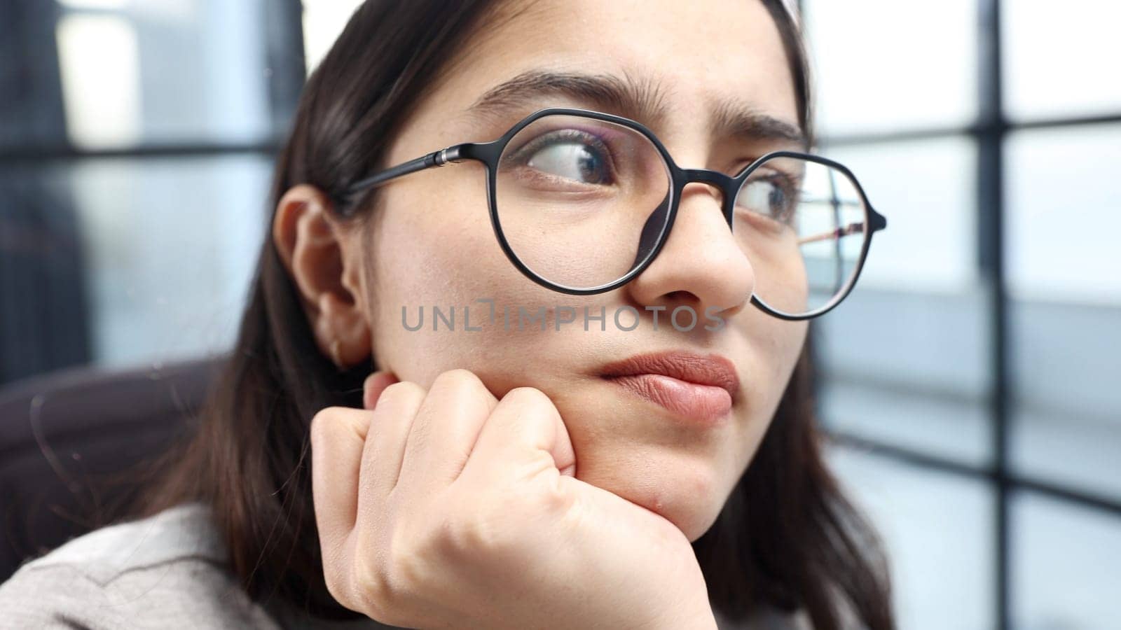 A young woman's face in close-up with glasses thinks.