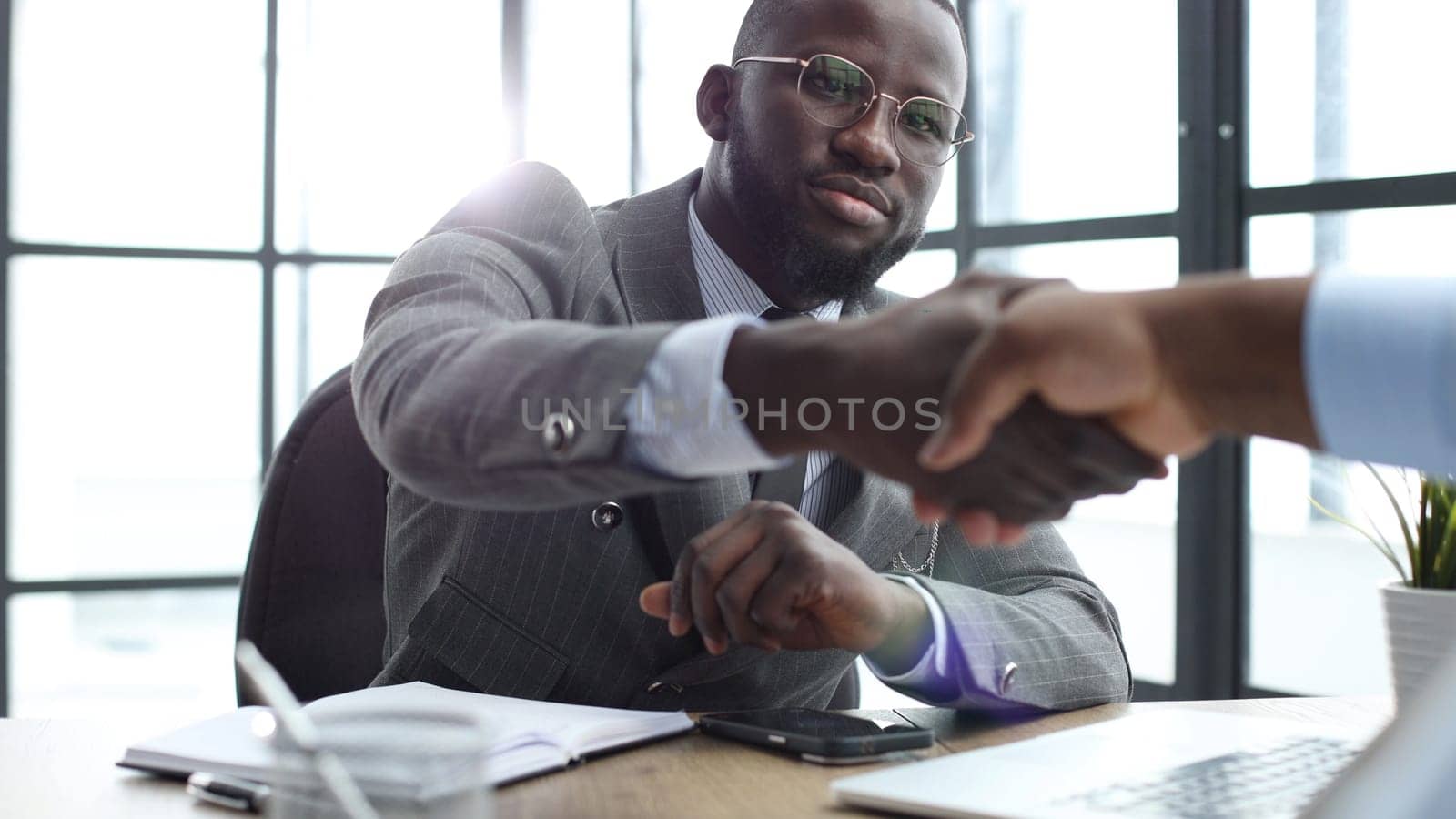 A businessman man in a close-up in a jacket shakes hands with a colleague in the office.