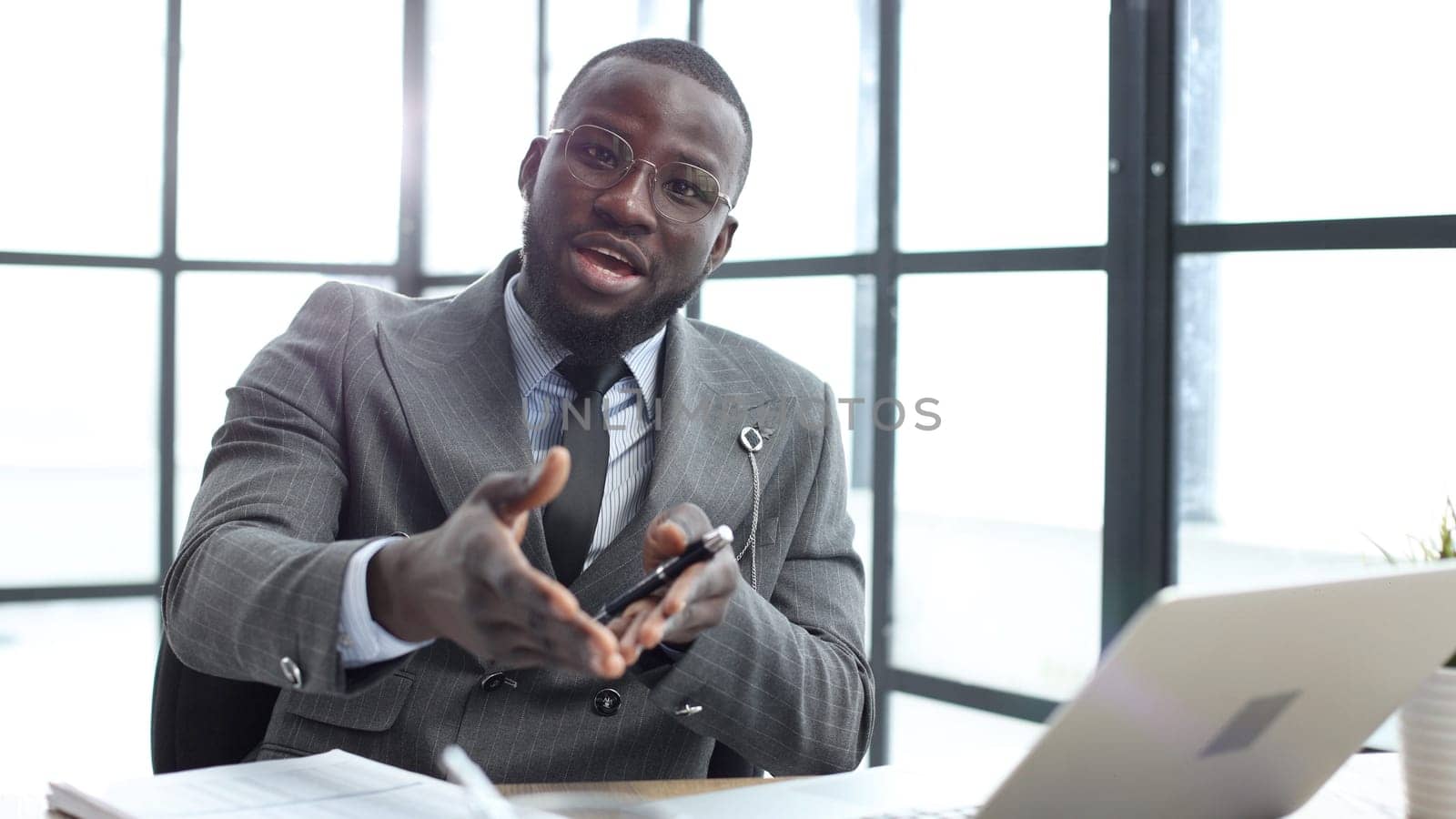 A businessman man in a close-up in a jacket speaks to the camera in the office.