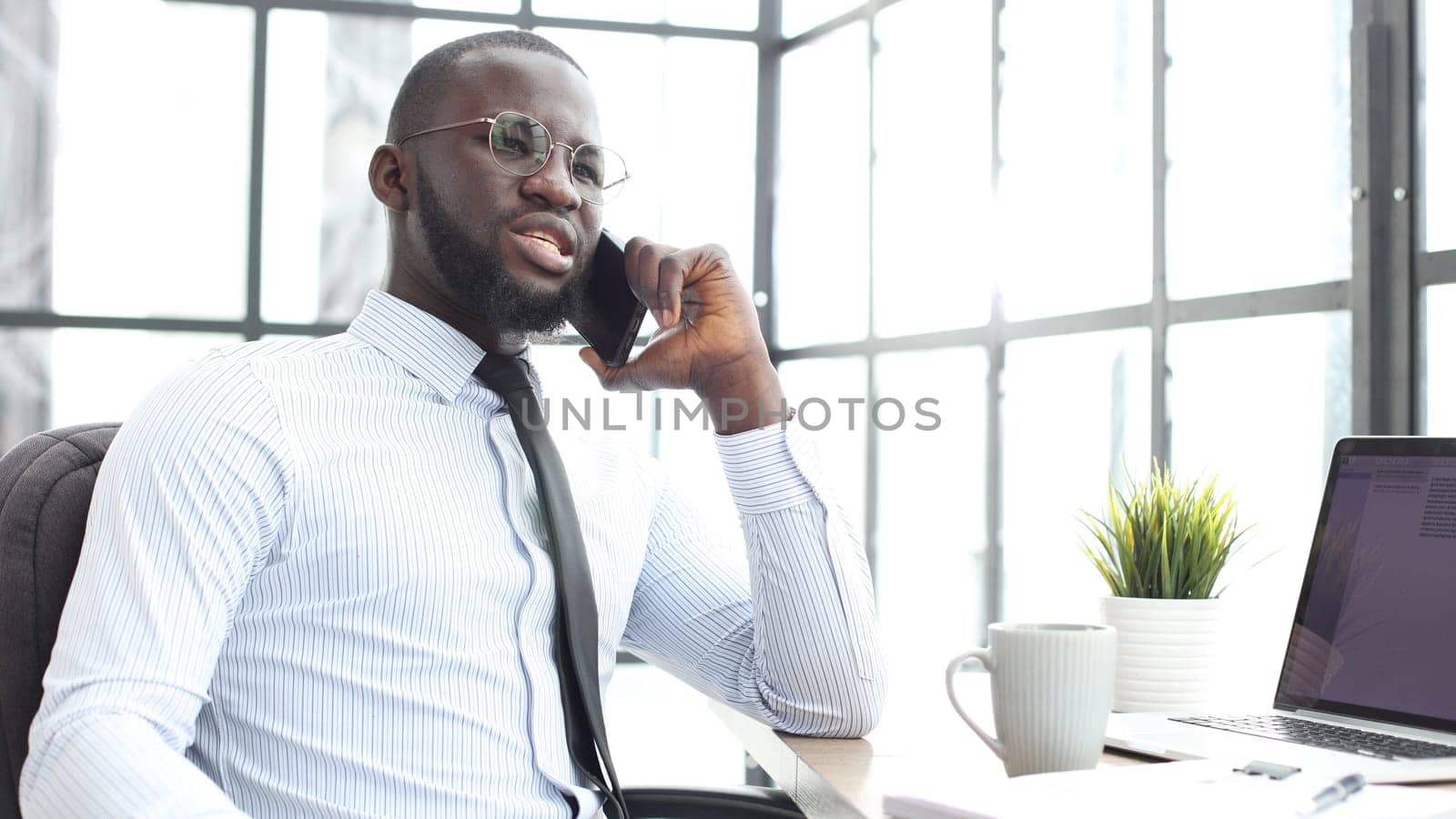 A businessman man in close-up in a shirt in the office talking on the phone.