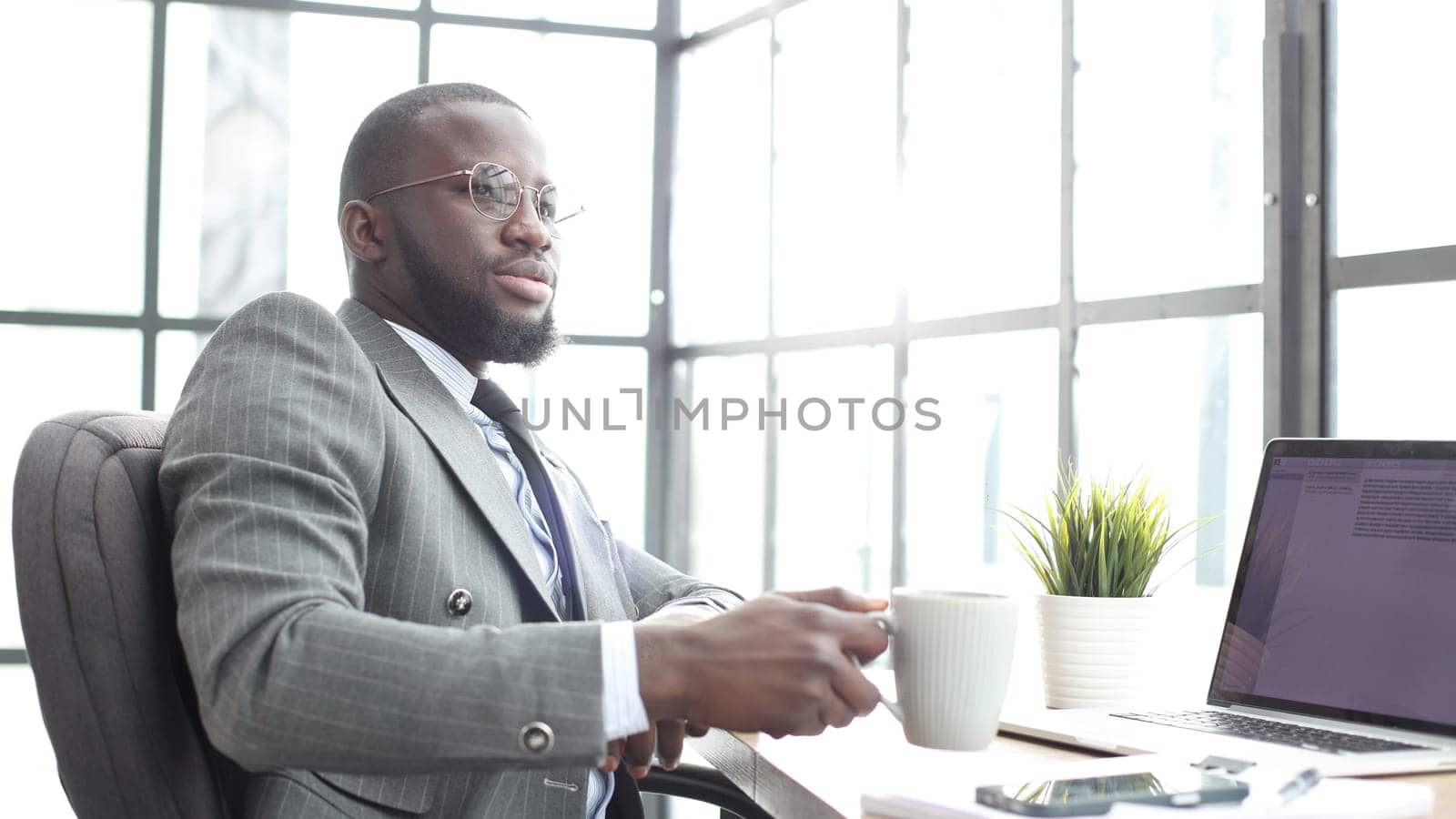 A businessman man in a close-up in a jacket in the office with a cup of coffee.