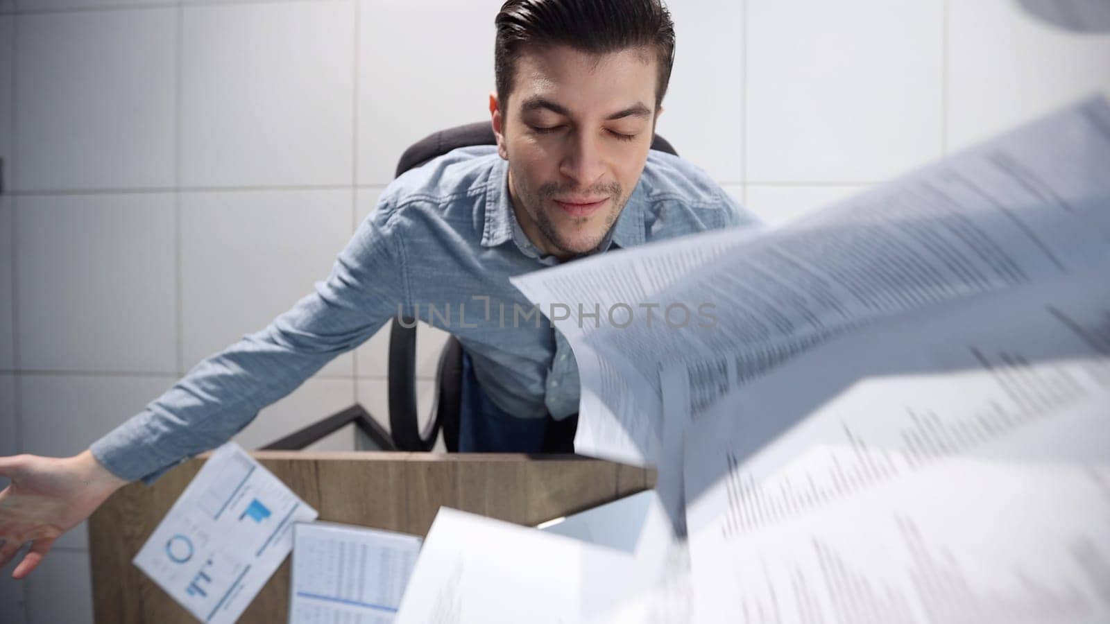 A male office worker is scattering papers.