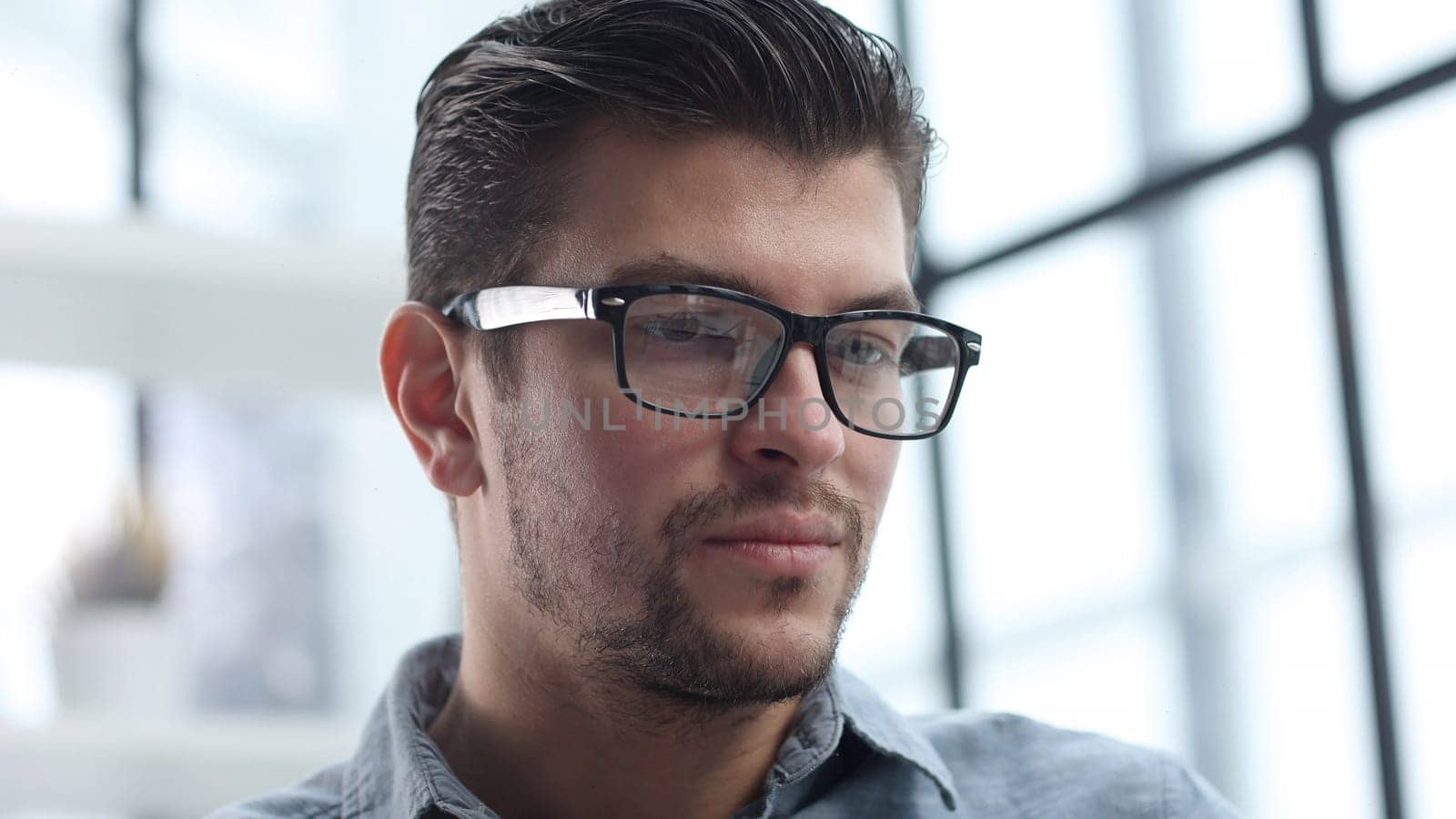 The man's face in glasses is in close-up, he looks thoughtfully away.