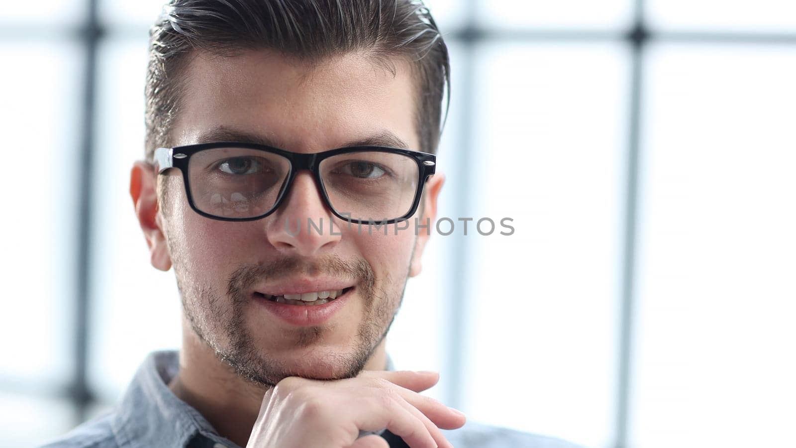 A man's face in close-up with glasses looks at the camera.