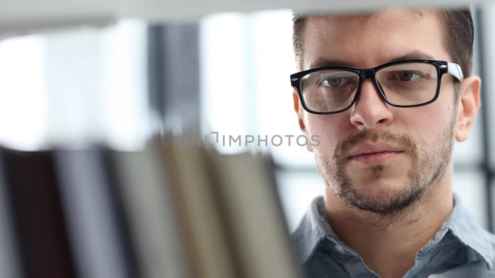 A man's face is in close-up with glasses, he is looking at books.