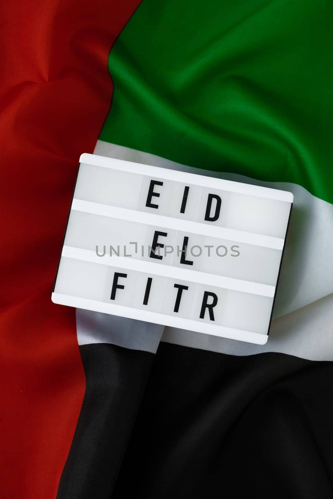 EID EL FITR - Eid Mubarak - Happy Holidays text frame on United Arab Emirates waving flag made from silk material. Public holiday celebration background. The National Flag of UAE. Patriotism Commemoration Day Muslim Ramadan Blessed Holy Month concept