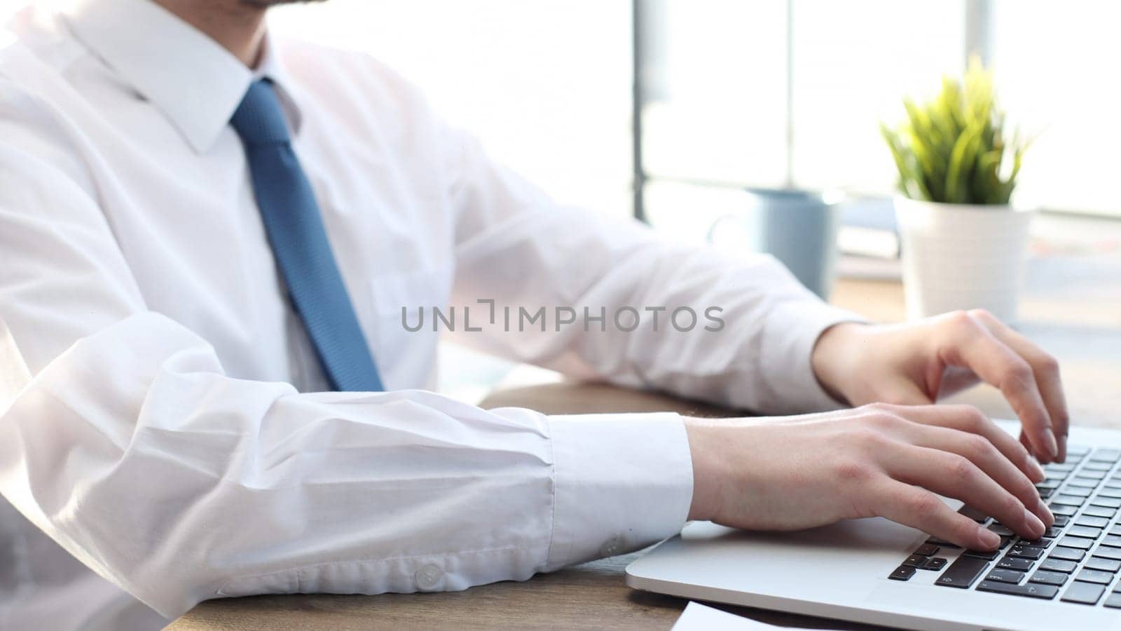 A businessman man in close-up in a shirt is typing on a laptop.