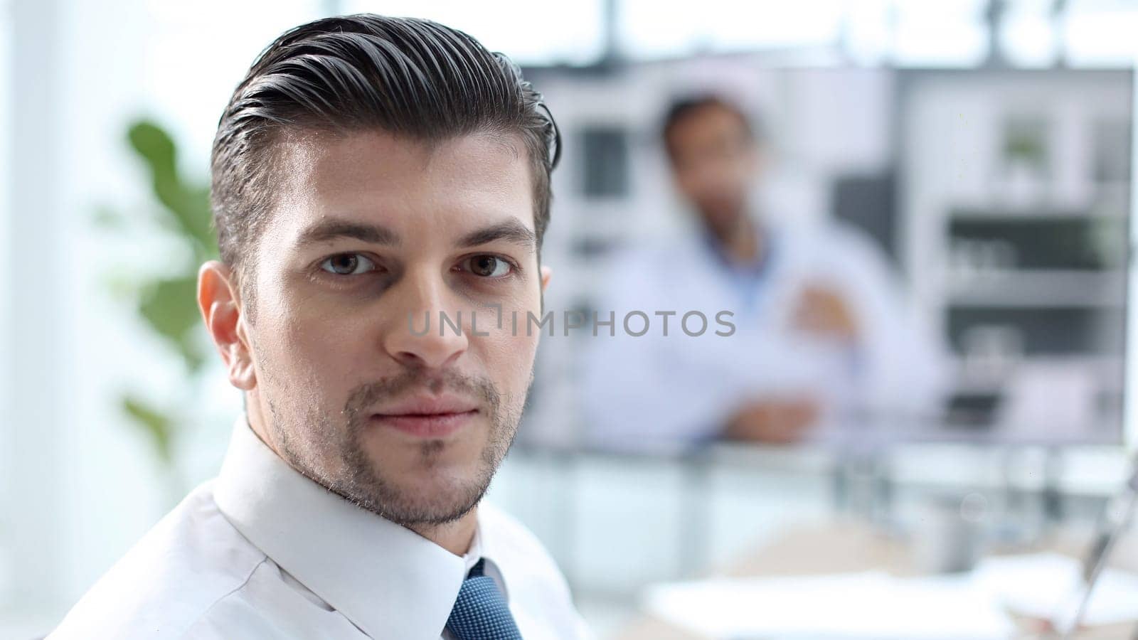 A male businessman is talking to colleagues at an online meeting and looking at camera by Prosto