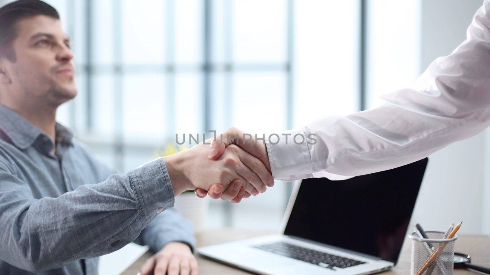 A male office worker shakes hands with a colleague in close-up.