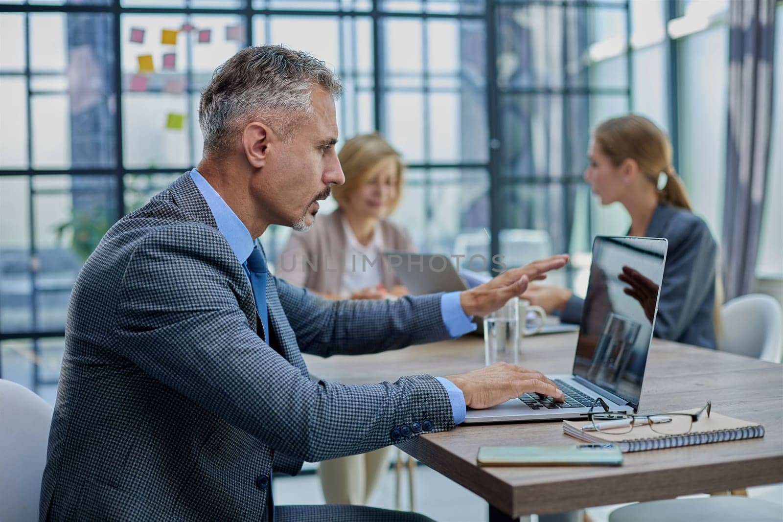 Confident businessman sitting at conference table in modern office by Prosto