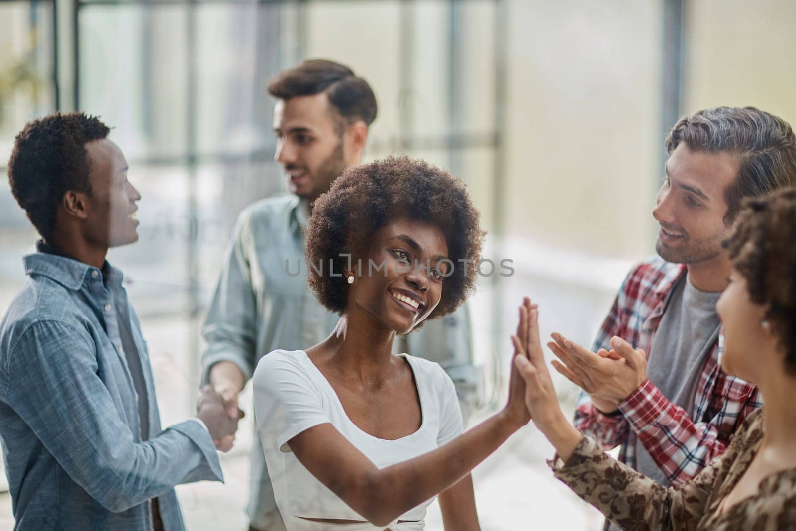 Excited multiracial employees give high five engaged in teambuilding activity in office together