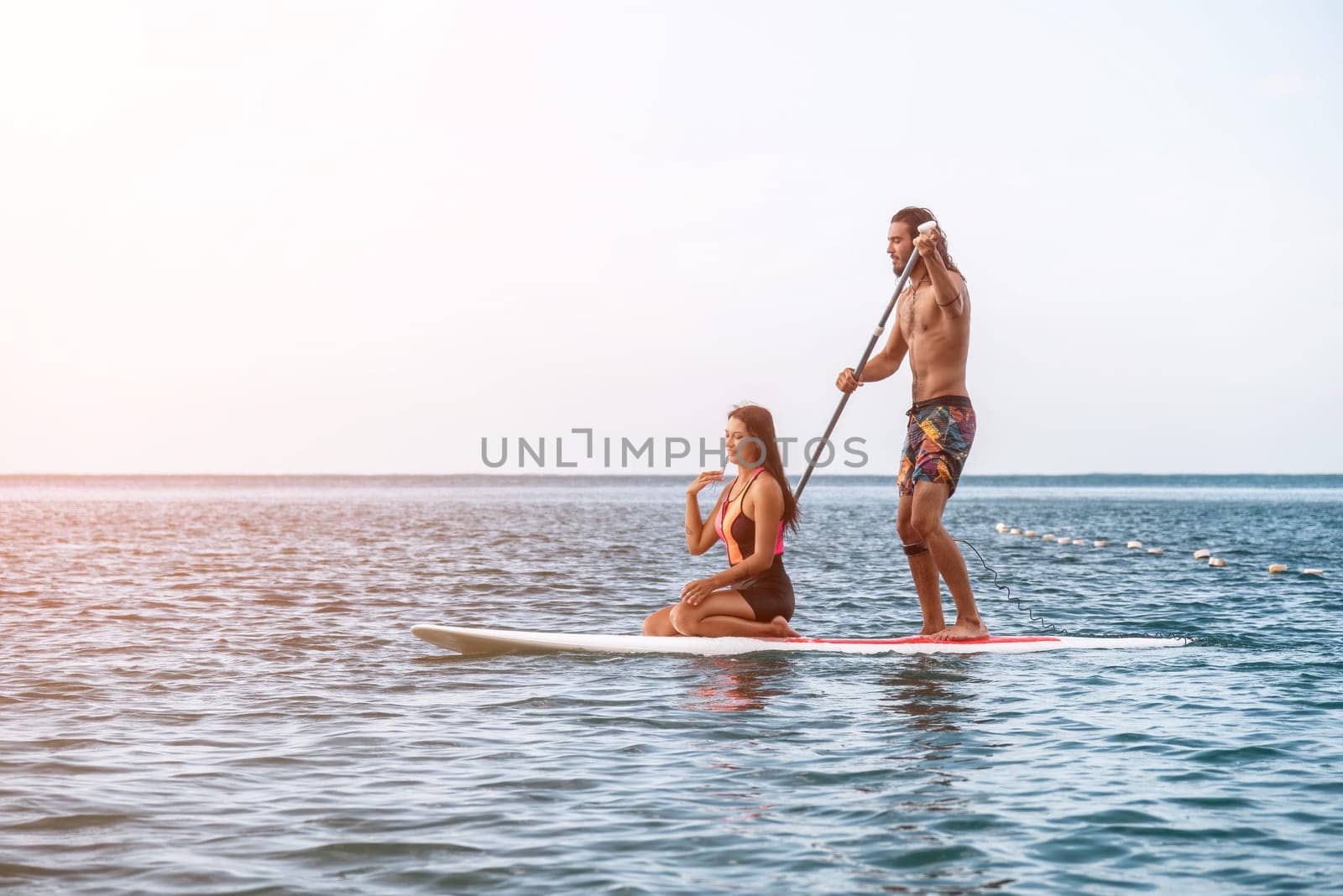 Sea woman and man on sup. Silhouette of happy young woman and man, surfing on SUP board, confident paddling through water surface. Idyllic sunset. Active lifestyle at sea or river