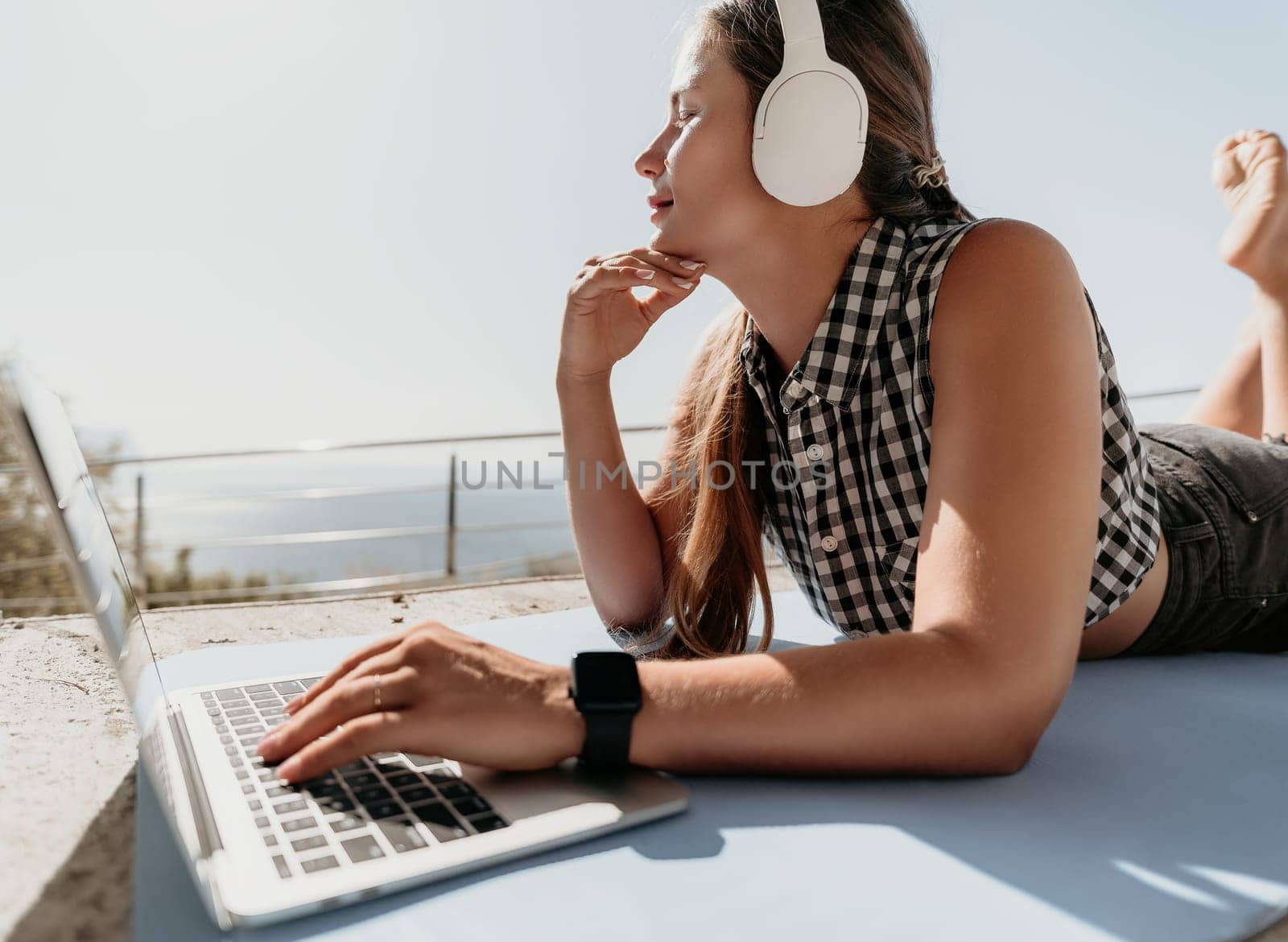 Woman laptop sea. Working remotely on seashore. Happy successful woman female freelancer working on laptop by the sea at sunset, makes a business transaction online. Freelance, remote work on vacation by panophotograph