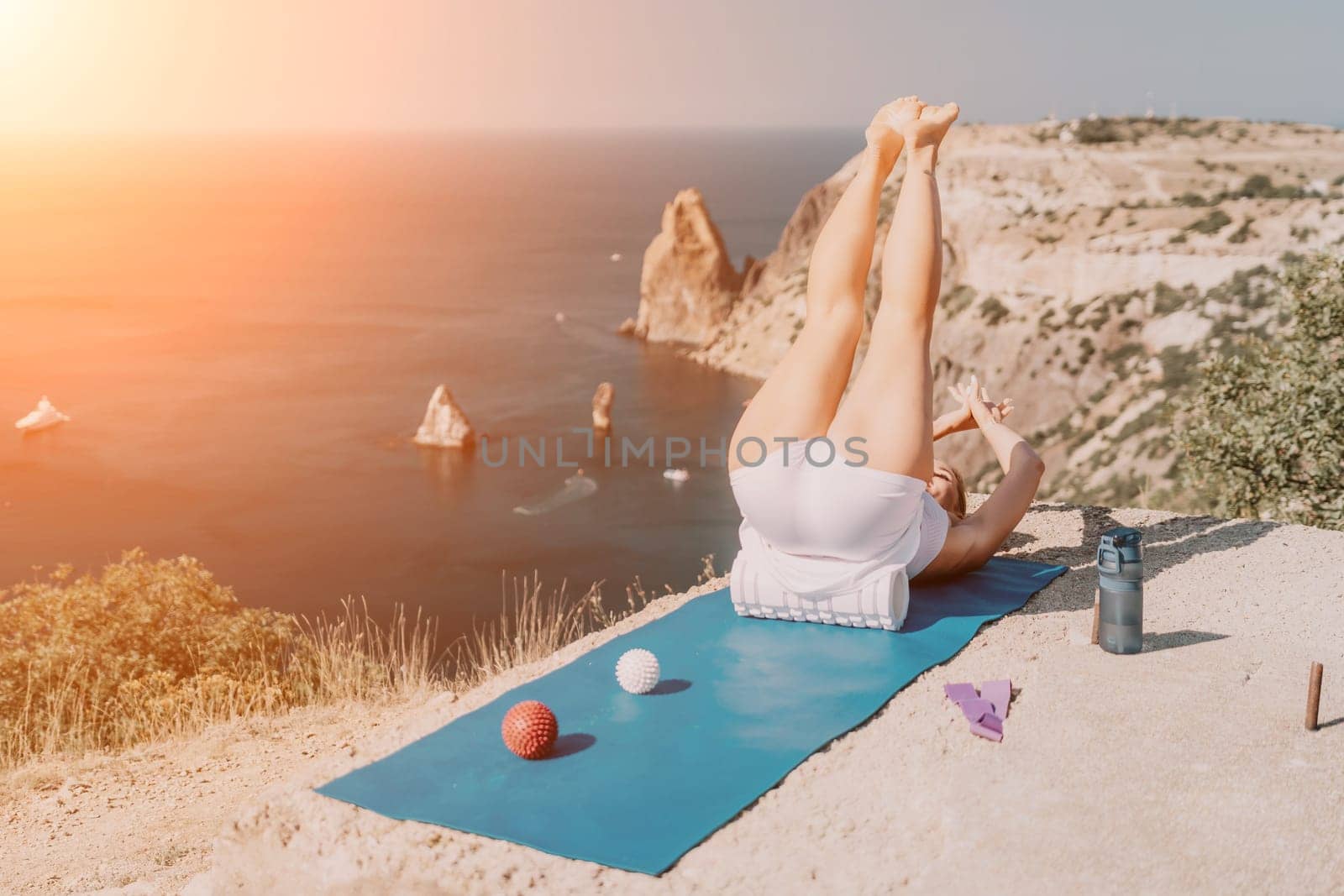 Woman sea pilates. Sporty happy middle aged woman practicing fitness on yoga mat with balls and roller near sea, smiling active female outside, enjoying healthy lifestyle, harmony and meditation. by panophotograph