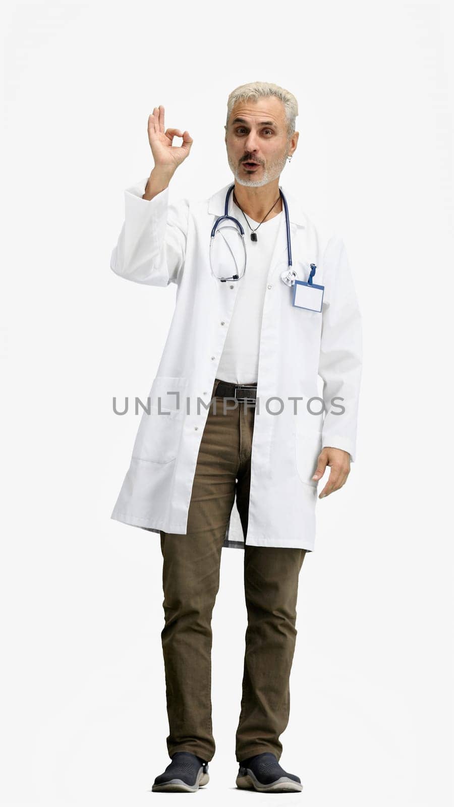 The doctor, in full height, on a white background, shows the ok sign.
