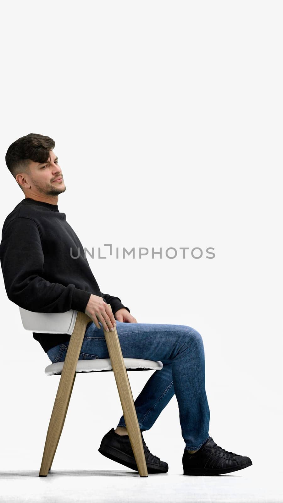 A man, on a white background, sitting on a chair.