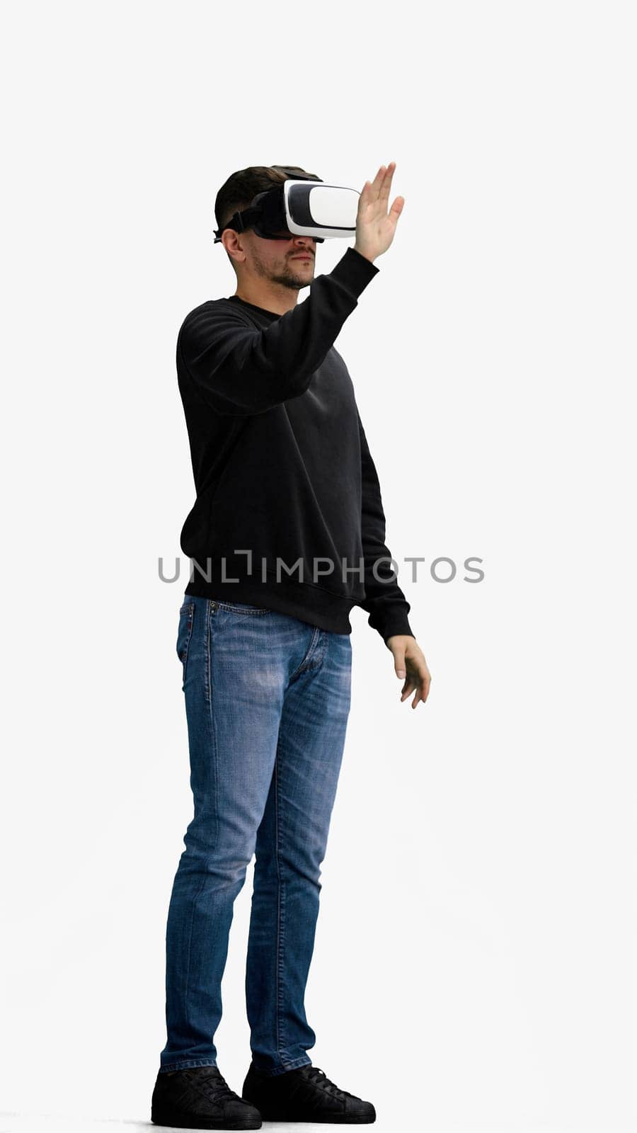 A man, full-length, on a white background, listening to music with headphones.
