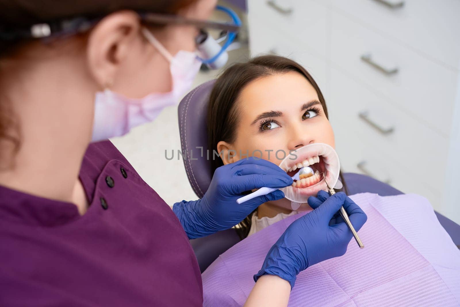 Female dentist checks oral cavity of patient using specialized mirror and tool for further treatment. Groundwork for effective dental treatment