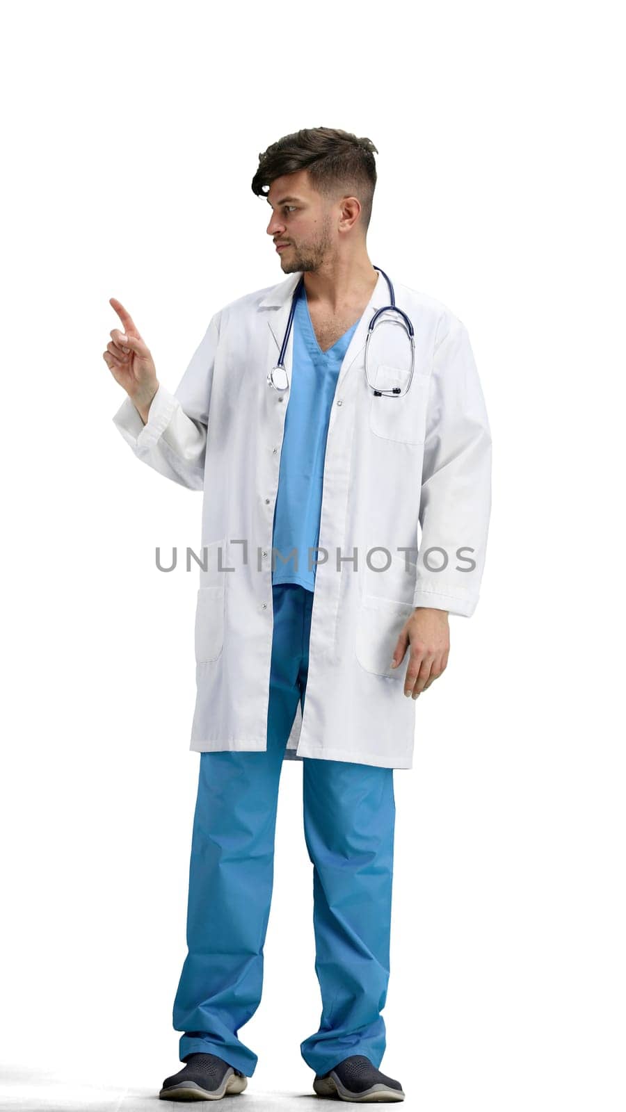 The doctor, in full height, on a white background, points to the side.