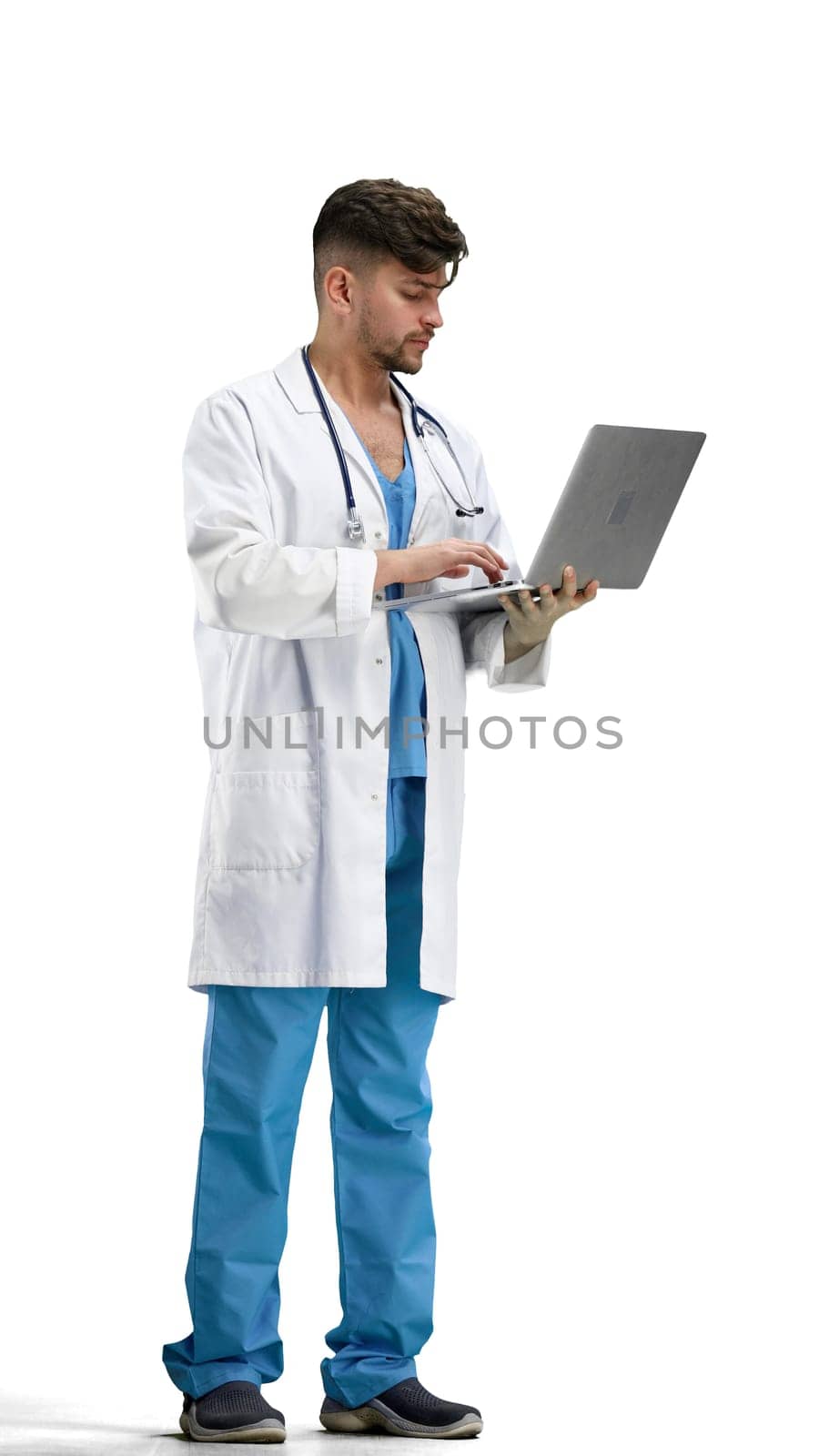 The doctor, in full height, on a white background, uses a laptop.