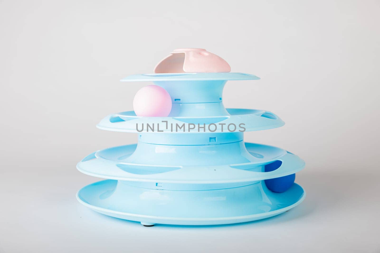 A playful cat on an isolated white background with a blue tower toy, circular turntable, and gripping a moving ball. Feline intelligence and hunter instincts define the fun.