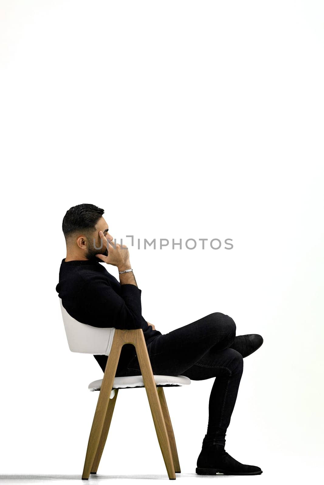 A man, full-length, on a white background, sitting on a chair.