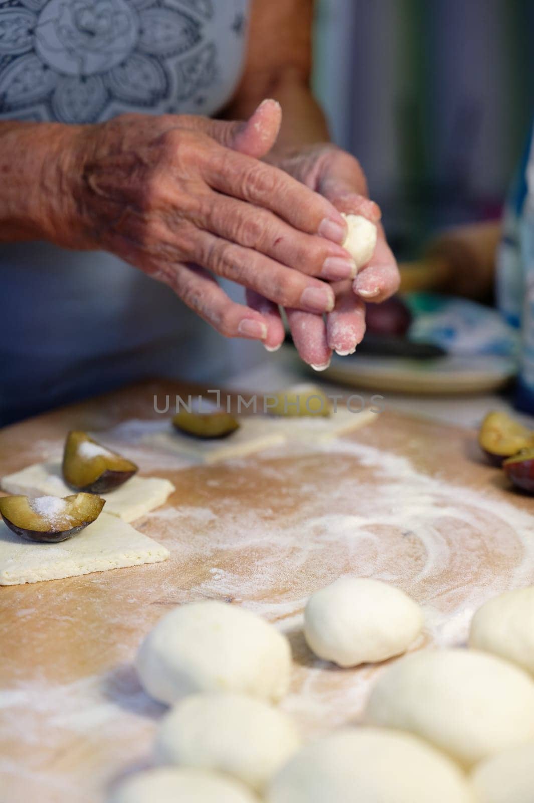 Preparation of homemade fruit dumplings with plums. Czech specialty of sweet good food. Dough on kitchen wooden table with hands.