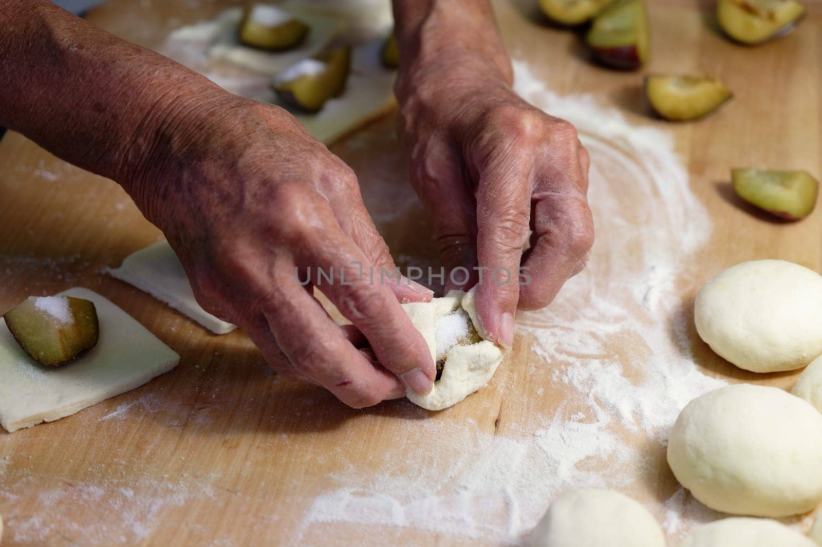 Preparation of homemade fruit dumplings with plums. Czech specialty of sweet good food. Dough on kitchen wooden table with hands.