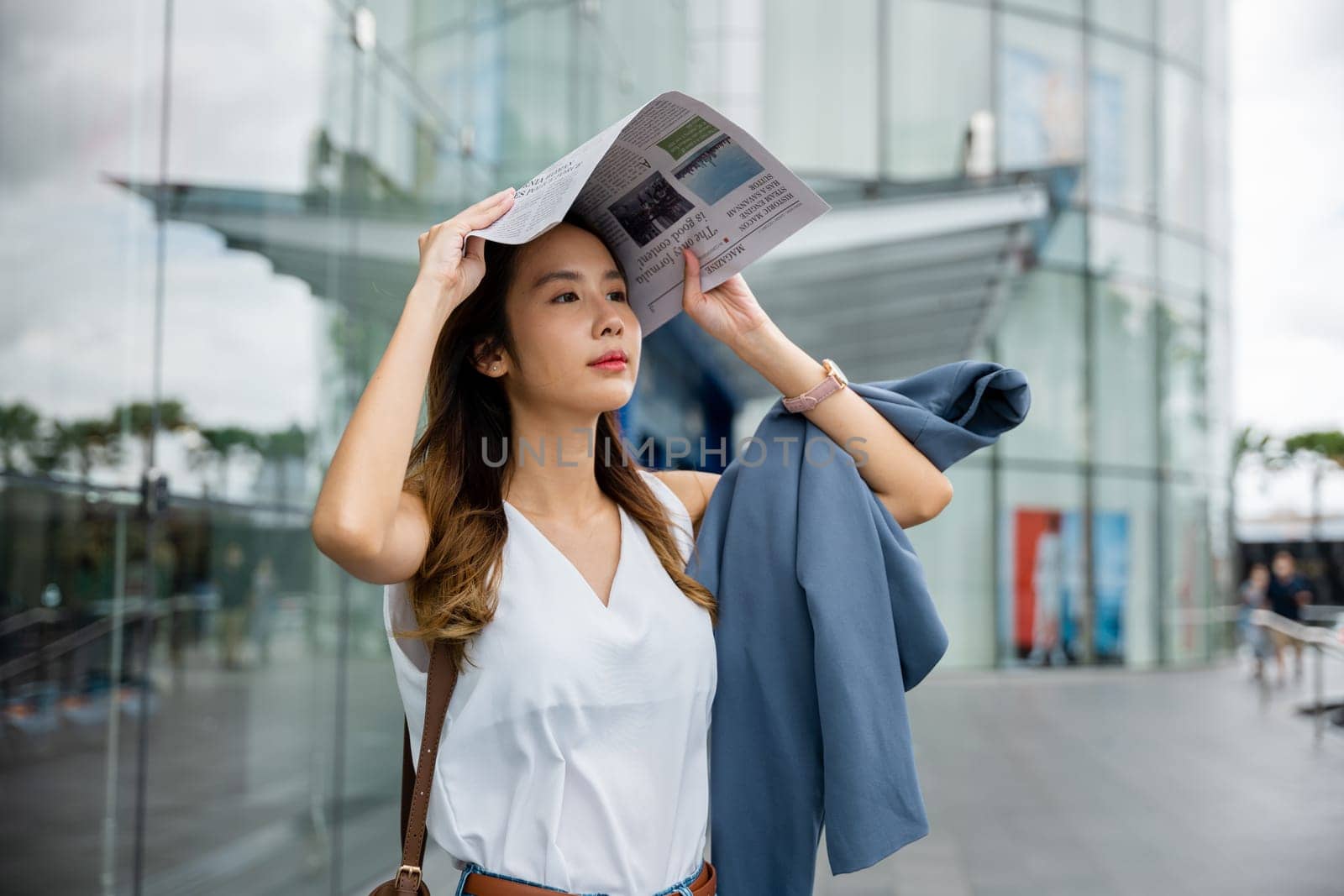 Overwhelmed by city living, an Asian woman covers her face with a newspaper by Sorapop