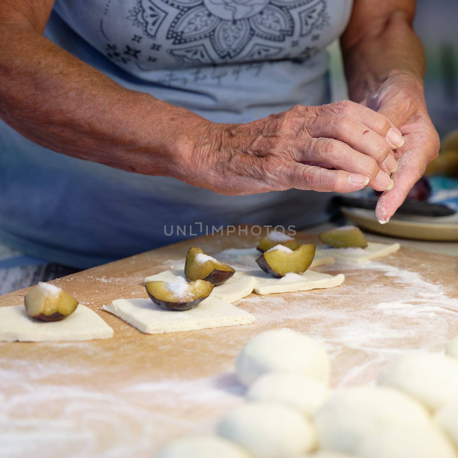 Preparation of homemade fruit dumplings with plums. Czech specialty of sweet good food. Dough on kitchen wooden table with hands. by Montypeter