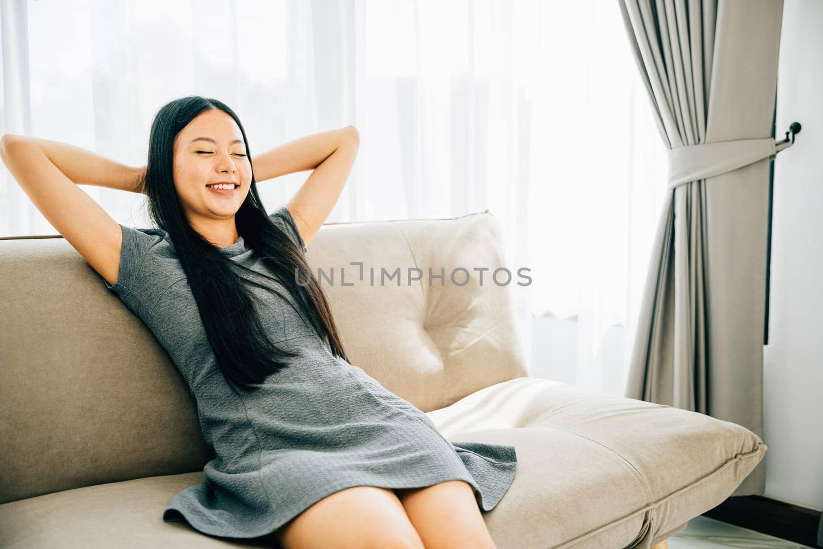 Relaxed woman on sofa hands behind head enjoys serene moment. Dreaming and finding balance in a cozy modern living room. Embracing relaxation wellbeing and mindfulness. Kick back and relax concept
