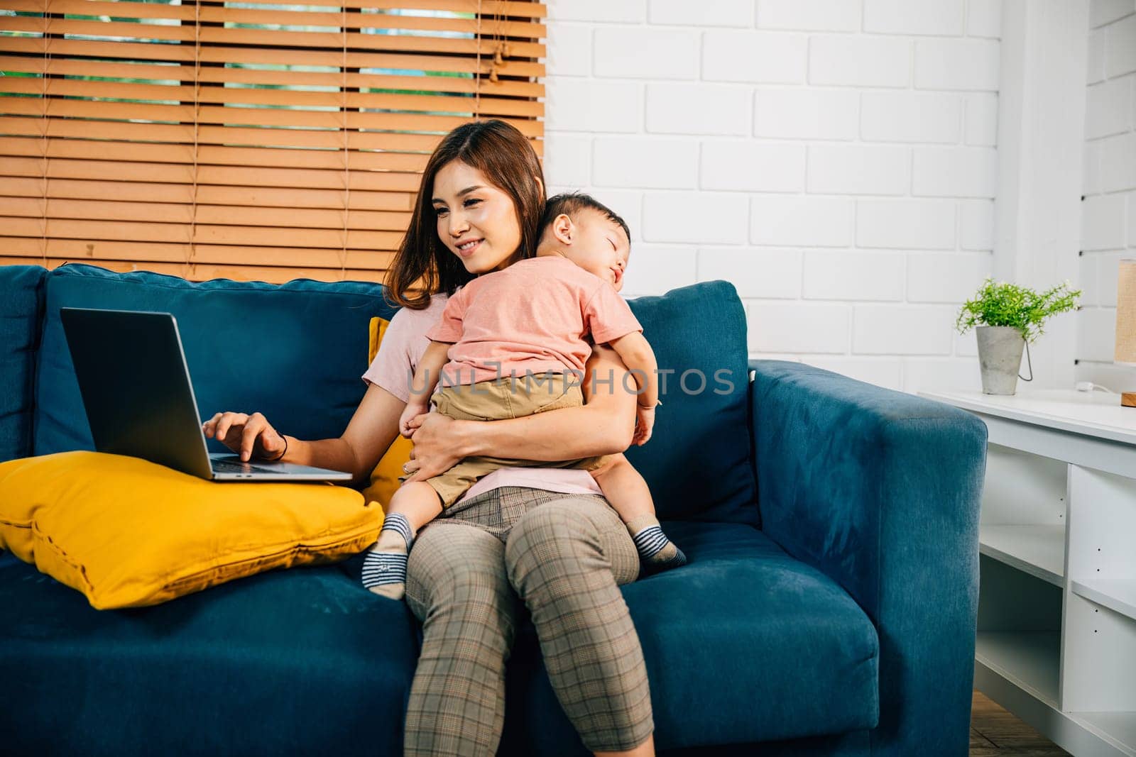 In a cozy home office a businesswoman focuses on her laptop while her baby daughter sleeps beside her. This portrait embodies the bond between a working mother and her child.