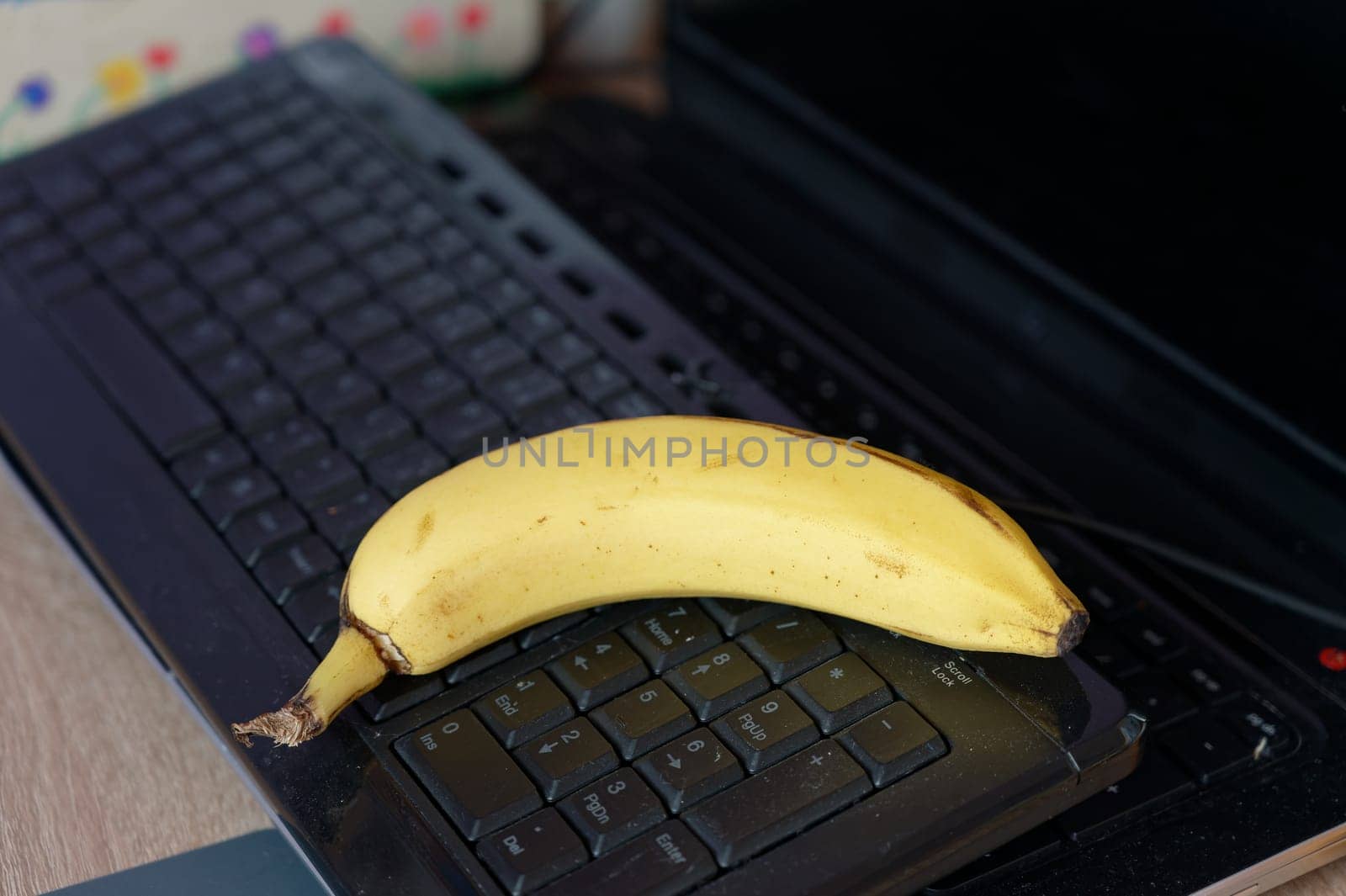 A beautiful fresh banana on a work table at home or in the office with a computer or laptop - notebook. by Montypeter