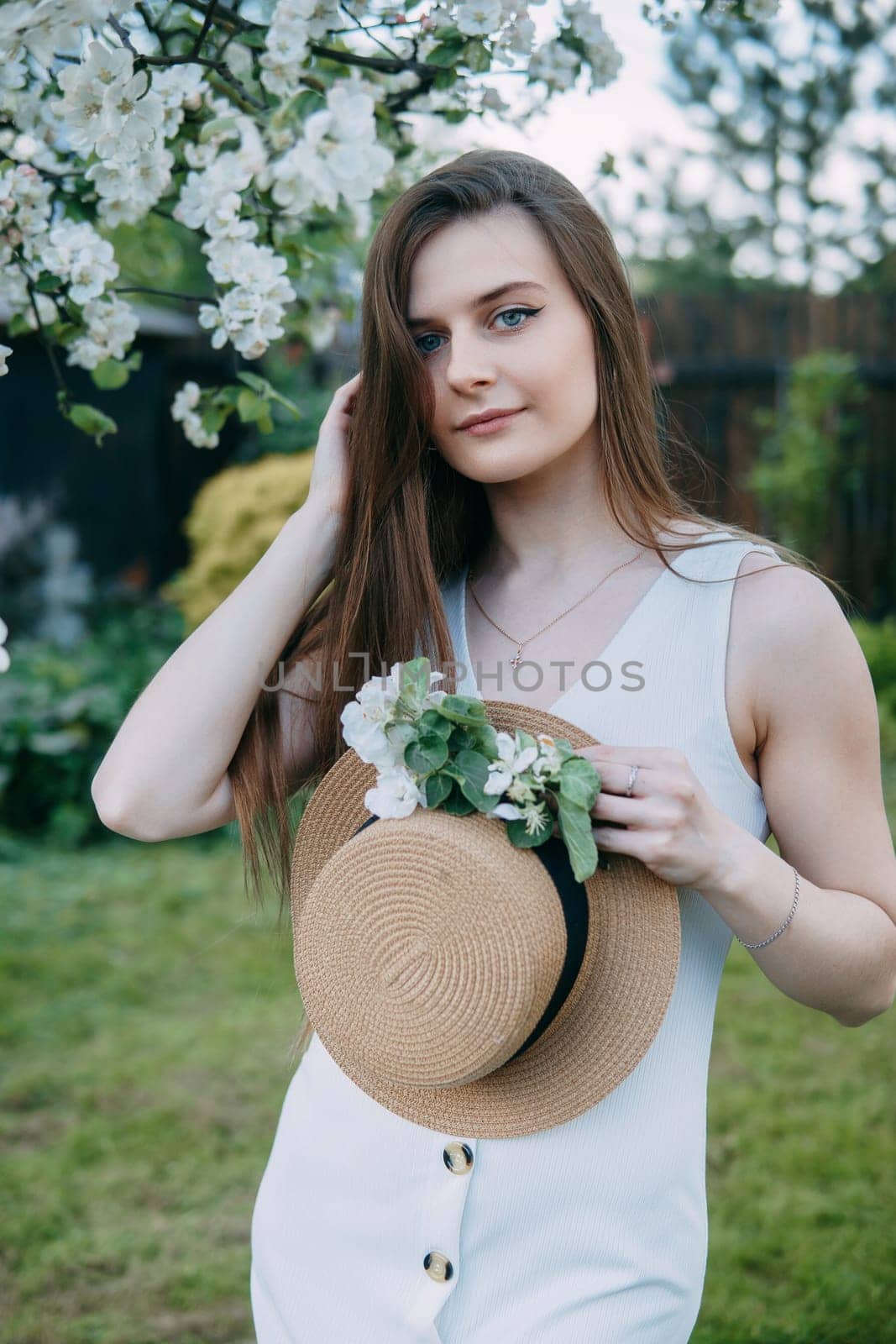 Beautiful young girl in white dress and hat in blooming Apple orchard. Blooming Apple trees with white flowers