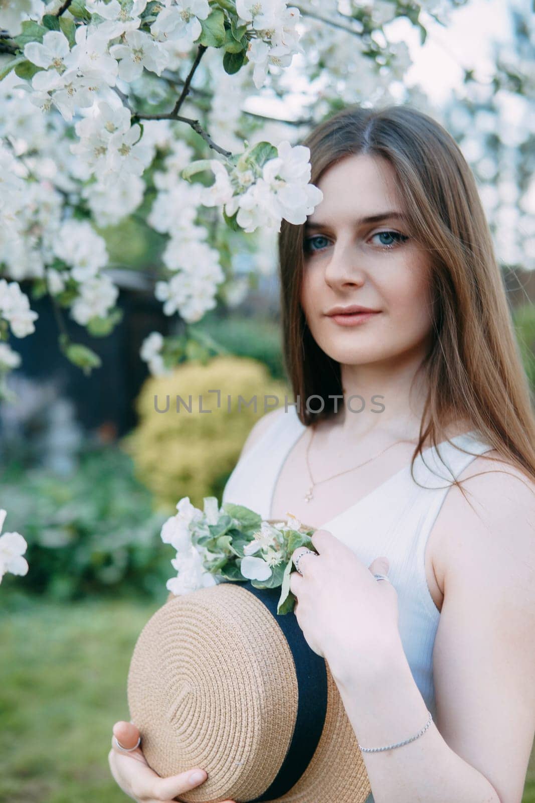 Beautiful young girl in white dress and hat in blooming Apple orchard. Blooming Apple trees with white flowers