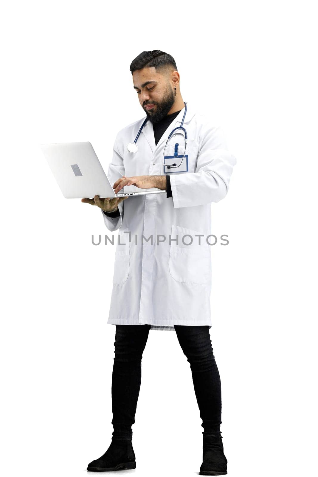 The doctor, in full height, on a white background, uses a laptop.