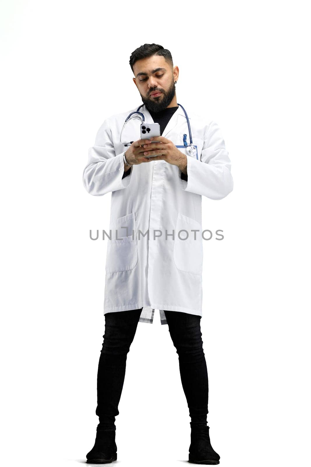 The doctor, in full height, on a white background, uses a phone.