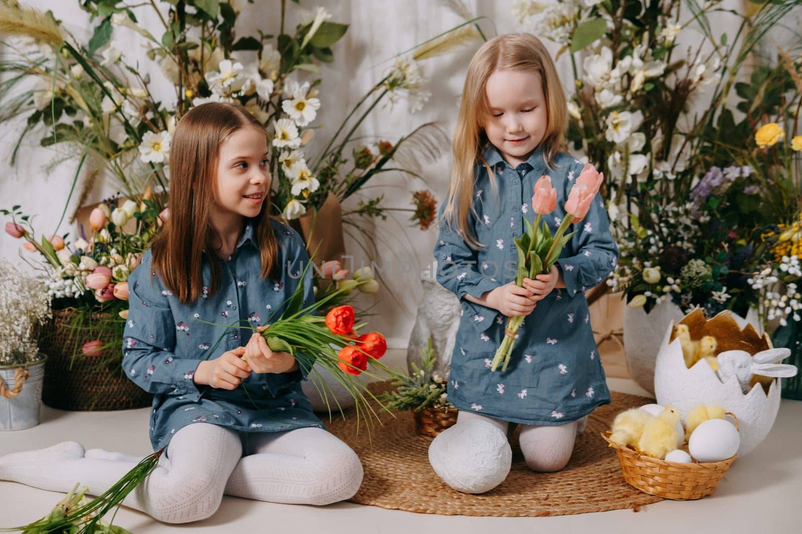 Two girls in a beautiful Easter photo zone with flowers, eggs, chickens and Easter bunnies. Happy Easter holiday. by Annu1tochka