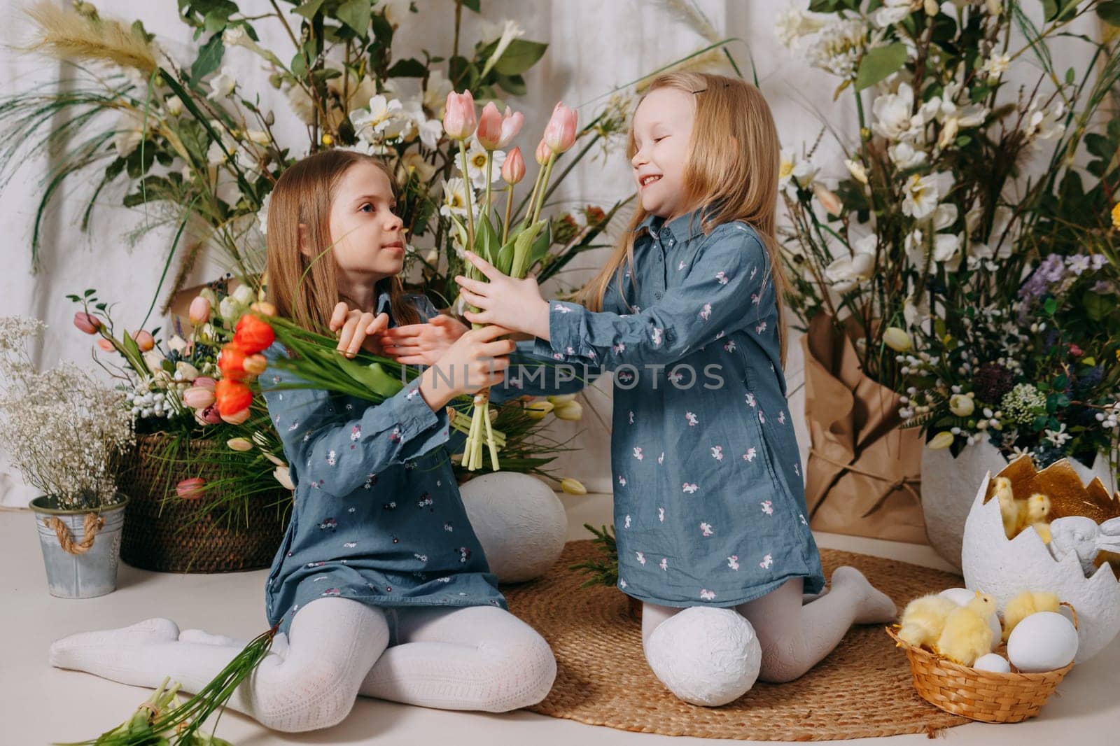 Two girls in a beautiful Easter photo zone with flowers, eggs, chickens and Easter bunnies. Happy Easter holiday. by Annu1tochka