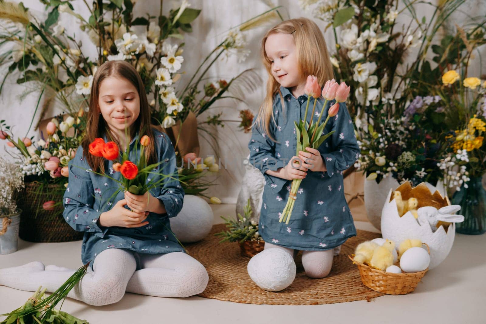 Two girls in a beautiful Easter photo zone with flowers, eggs, chickens and Easter bunnies. Happy Easter holiday. by Annu1tochka