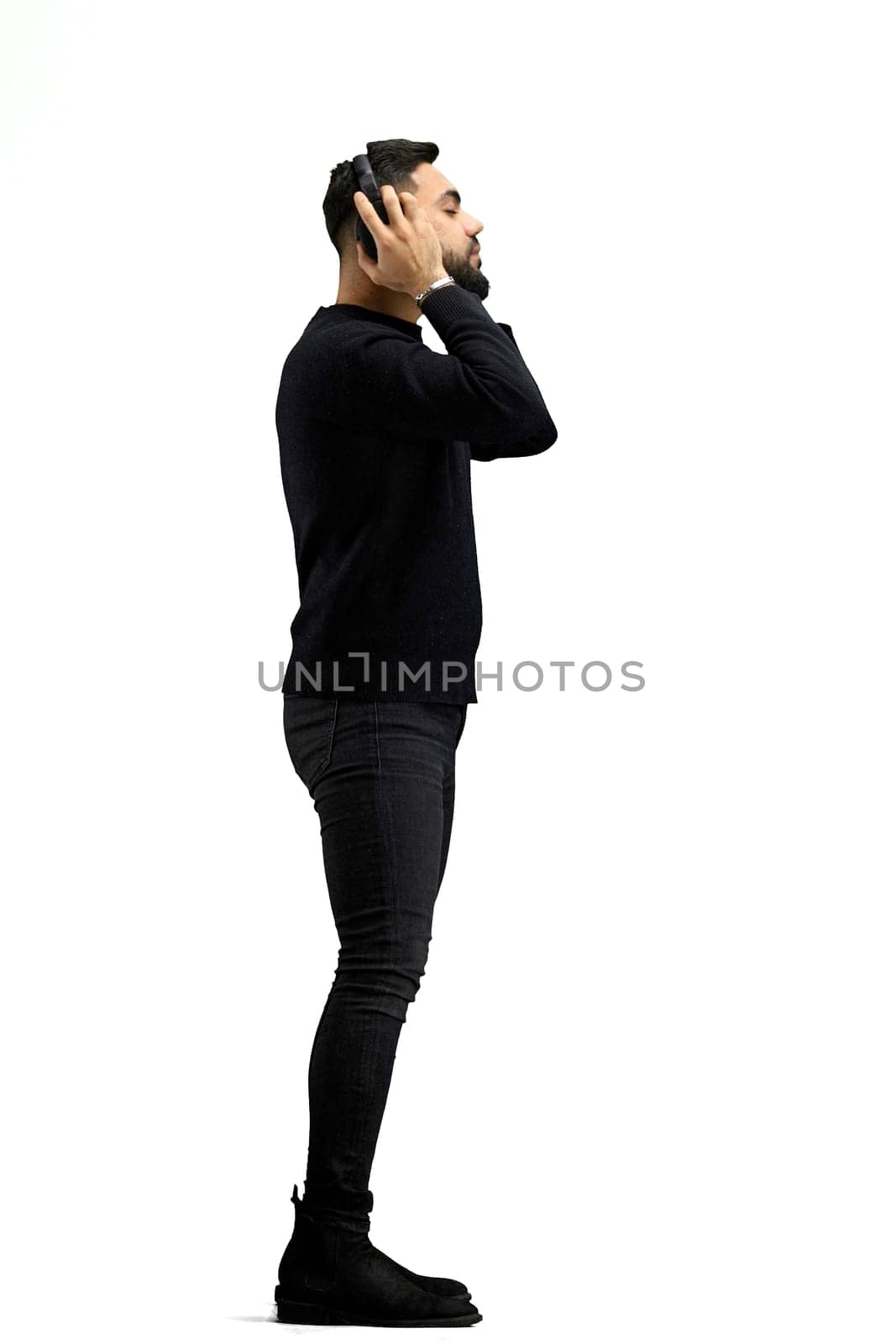 A man, in full height, on a white background, listens to music with headphones.