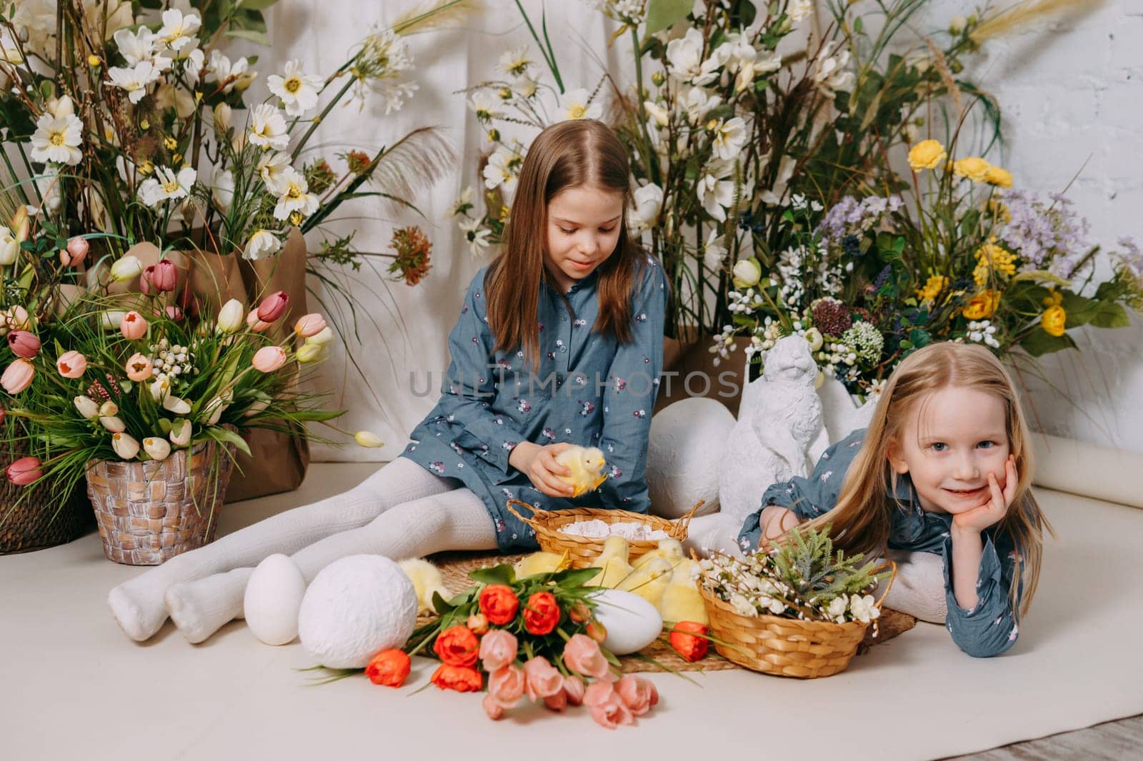 Two girls in a beautiful Easter photo zone with flowers, eggs, chickens and Easter bunnies. Happy Easter holiday. by Annu1tochka