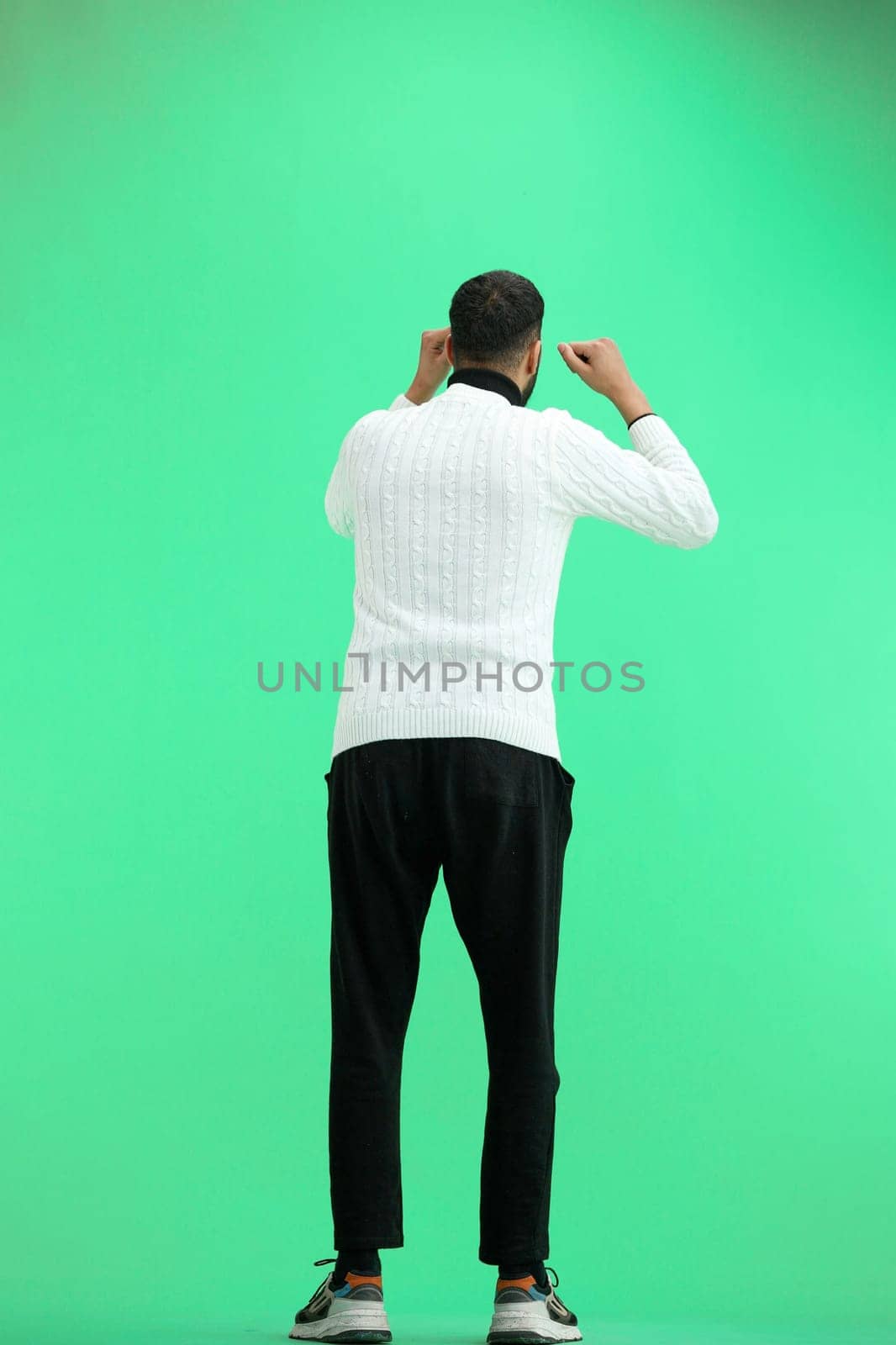 A man, full-length, on a green background, raised his hands up.