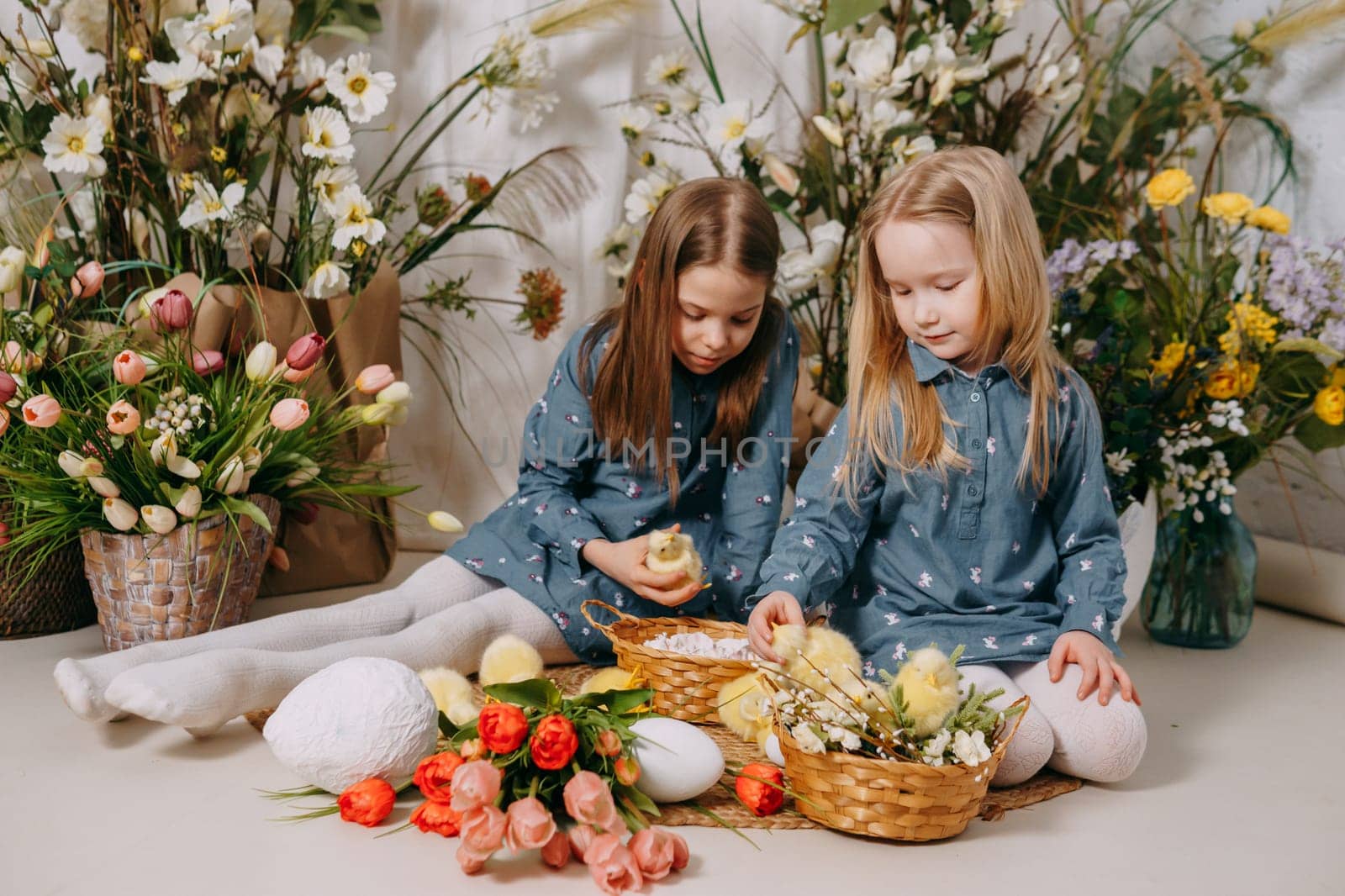 Two girls in a beautiful Easter photo zone with flowers, eggs, chickens and Easter bunnies. Happy Easter holiday