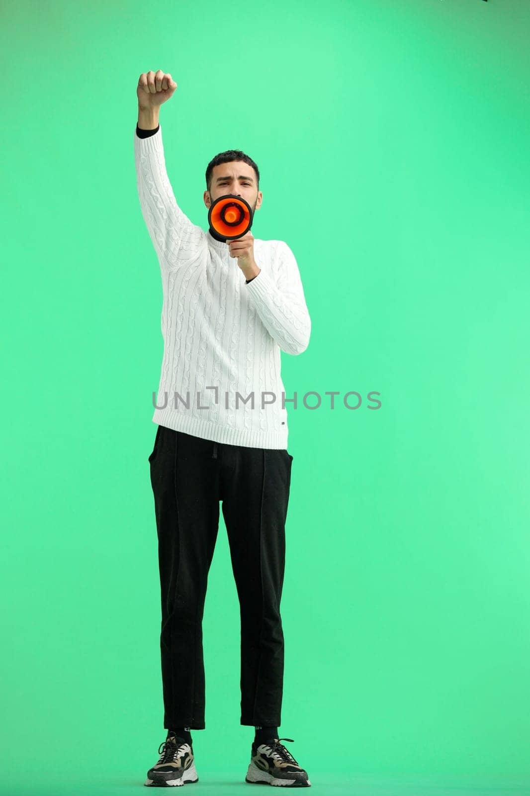 A man, full-length, on a green background, with a megaphone.